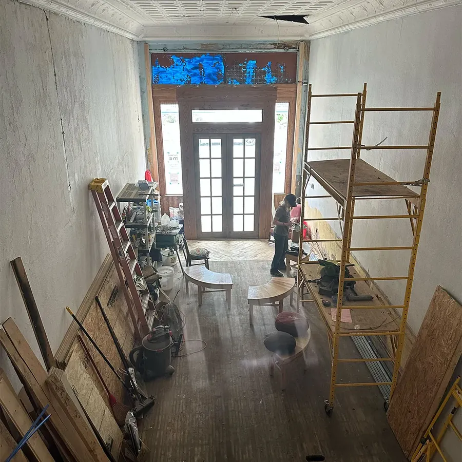 The long, narrow shop interior during renovation, with ladders and scaffolding