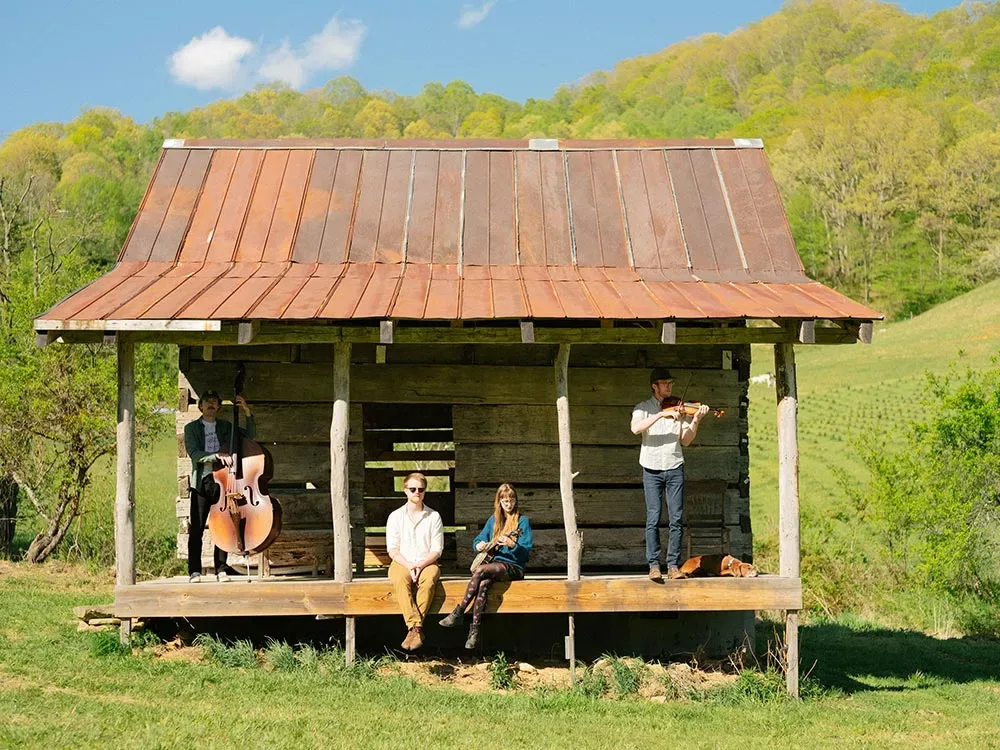 The Holler Choir on the porch of an old log cabin, with green mountains behind them
