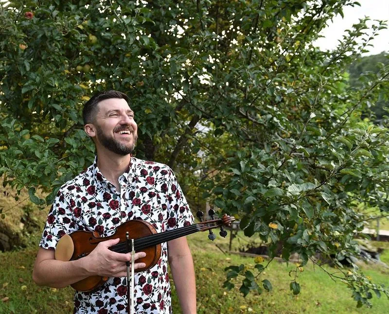 Fiddler Josh Goforth smiling in an apple orchard