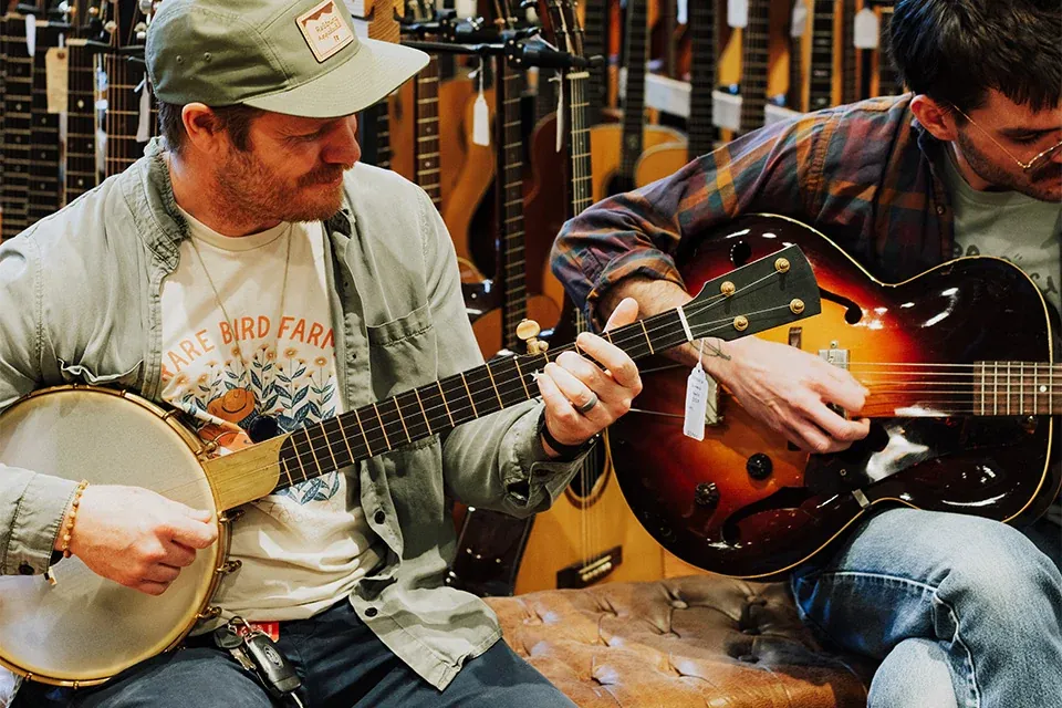 Two musicians trying a banjo and an archtop guitar in a music shop