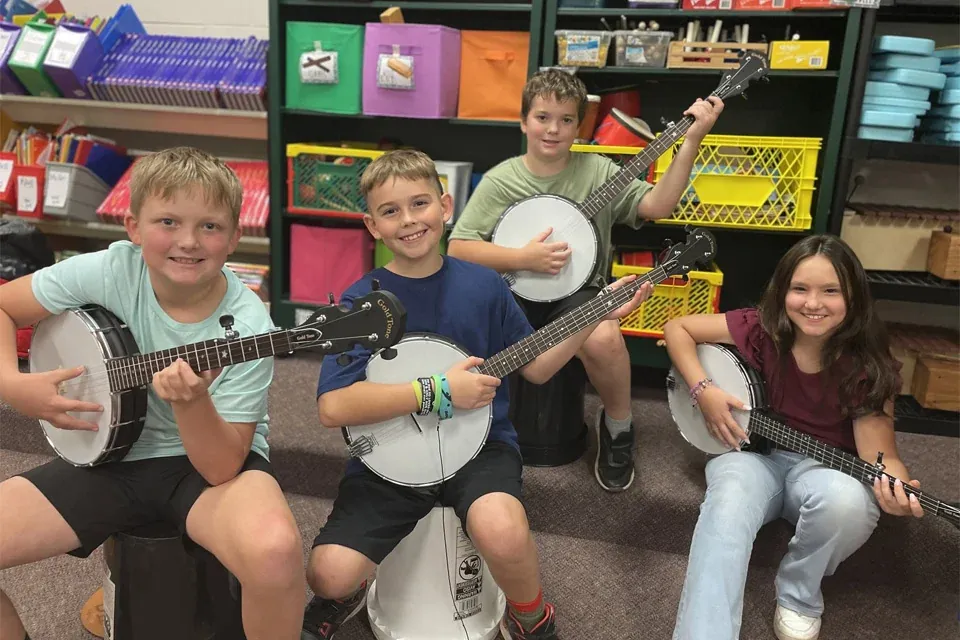 Three young players holding banjos at a workshop